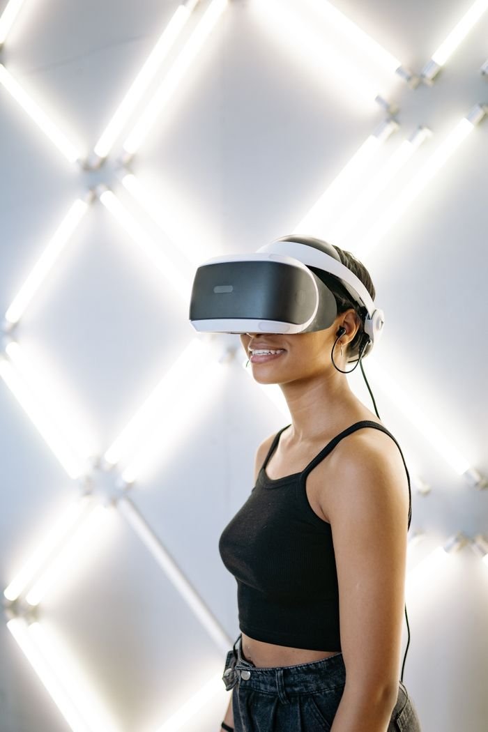 Young woman in a black tank top enjoying a virtual reality game with VR goggles in a studio.
